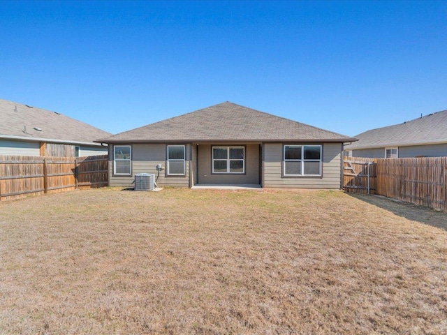rear view of house featuring roof with shingles, a yard, a fenced backyard, and central AC unit