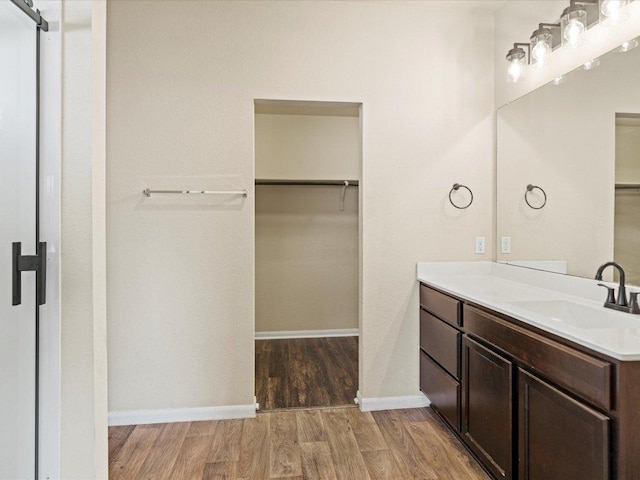 full bathroom with a spacious closet, vanity, wood finished floors, and baseboards