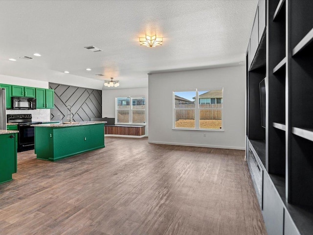 kitchen with wood finished floors, visible vents, a center island with sink, green cabinetry, and black appliances