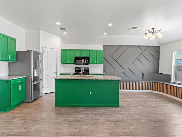 kitchen with an island with sink, green cabinets, visible vents, black appliances, and light wood finished floors