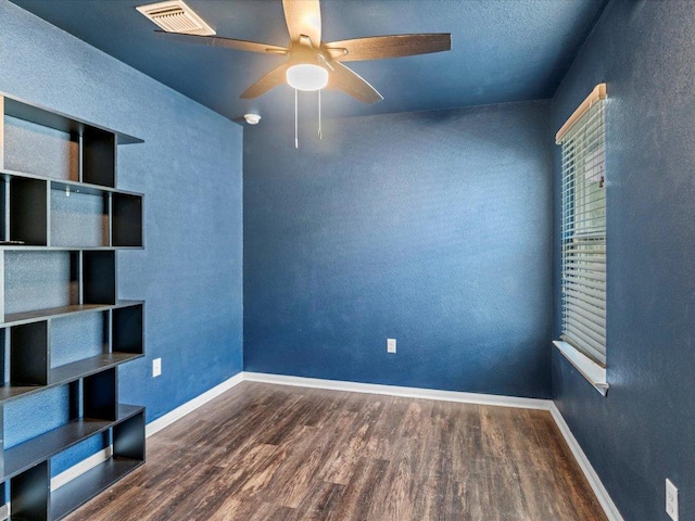 empty room with visible vents, baseboards, wood finished floors, a textured wall, and a ceiling fan