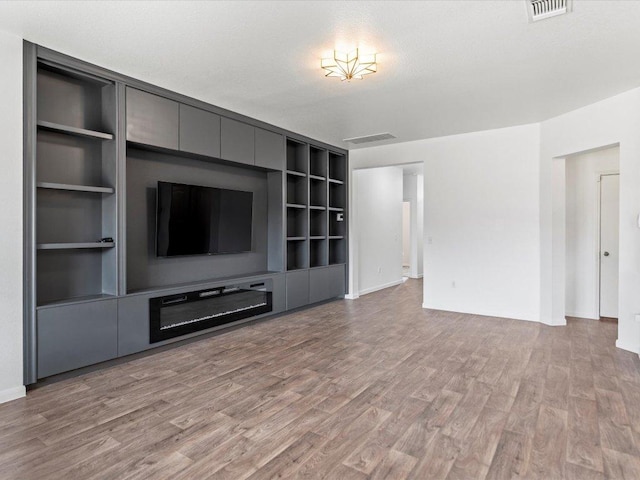 unfurnished living room with visible vents, light wood-style flooring, built in shelves, and a textured ceiling