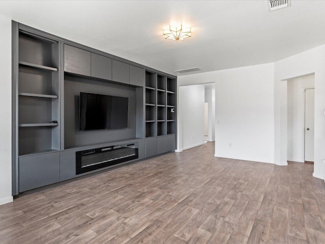 unfurnished living room featuring light wood-style floors, built in features, and visible vents