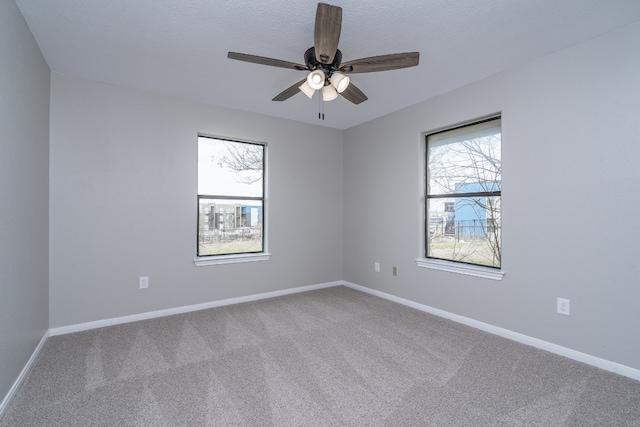 carpeted spare room with plenty of natural light, a textured ceiling, a ceiling fan, and baseboards