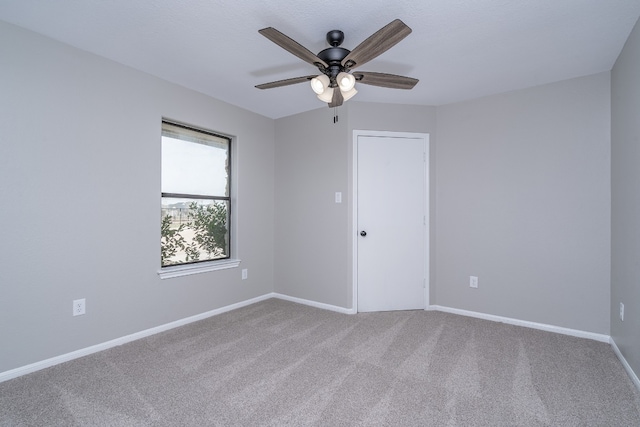 carpeted spare room featuring a ceiling fan and baseboards