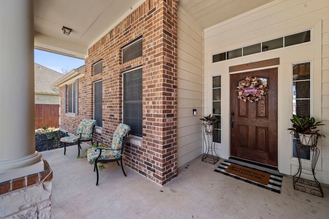 view of exterior entry with brick siding and a porch