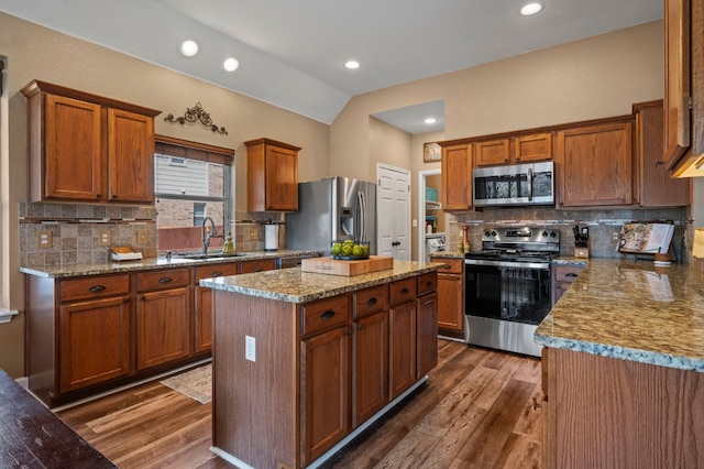 kitchen with a sink, a center island, stainless steel appliances, dark wood-style flooring, and vaulted ceiling