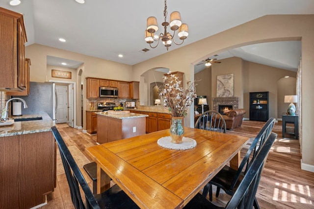 dining room with visible vents, lofted ceiling, light wood-style flooring, arched walkways, and a brick fireplace