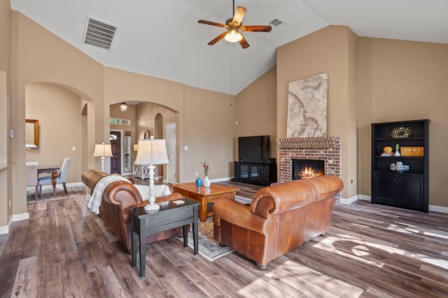 living area featuring visible vents, high vaulted ceiling, a brick fireplace, and wood finished floors