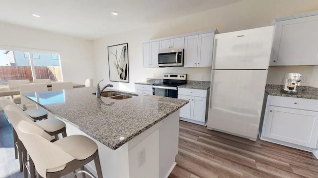 kitchen with a kitchen bar, a sink, wood finished floors, appliances with stainless steel finishes, and light stone countertops