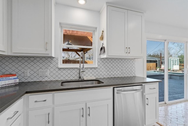 kitchen with a sink, backsplash, dark countertops, white cabinets, and dishwasher