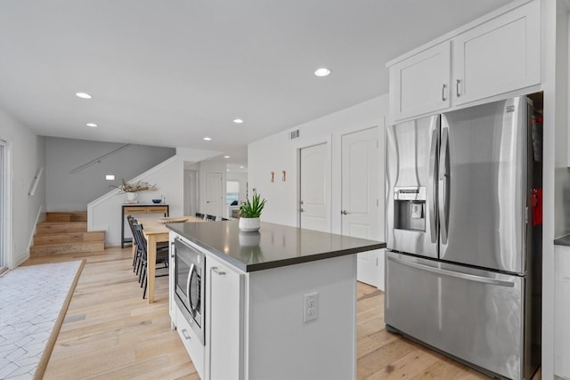 kitchen with dark countertops, a kitchen island, white cabinetry, appliances with stainless steel finishes, and light wood finished floors