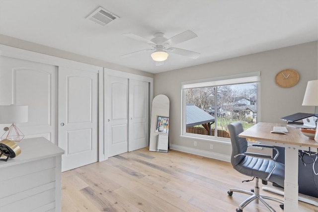 home office with light wood-style flooring, a ceiling fan, visible vents, and baseboards