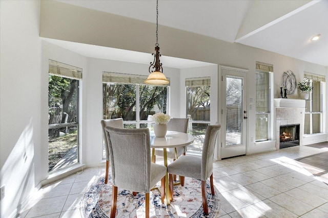 dining space featuring light tile patterned flooring, a healthy amount of sunlight, a tiled fireplace, and lofted ceiling