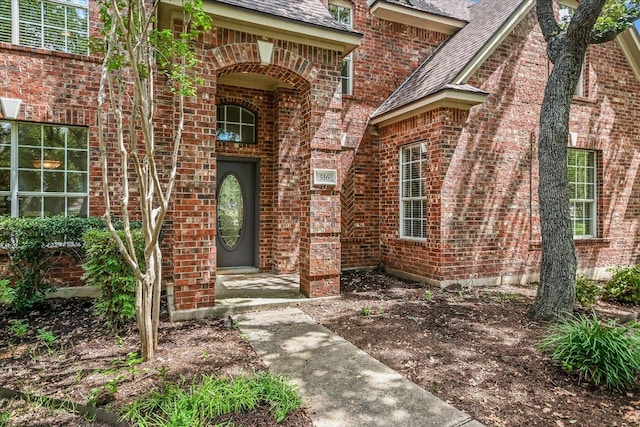 property entrance featuring brick siding and a shingled roof