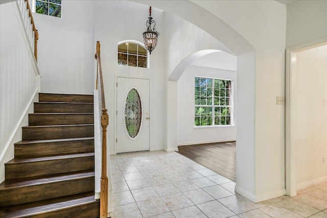 foyer with baseboards, a chandelier, stairway, light tile patterned floors, and a high ceiling