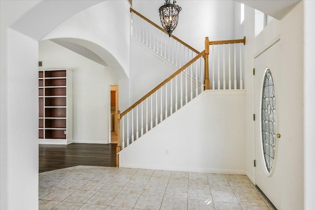 foyer with tile patterned floors, a notable chandelier, a high ceiling, and baseboards