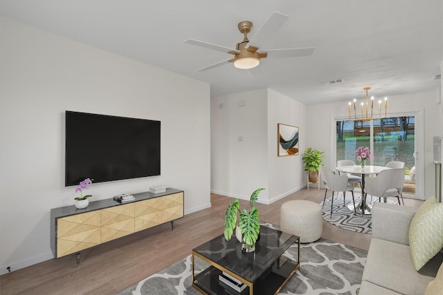 living area with visible vents, baseboards, wood finished floors, and ceiling fan with notable chandelier