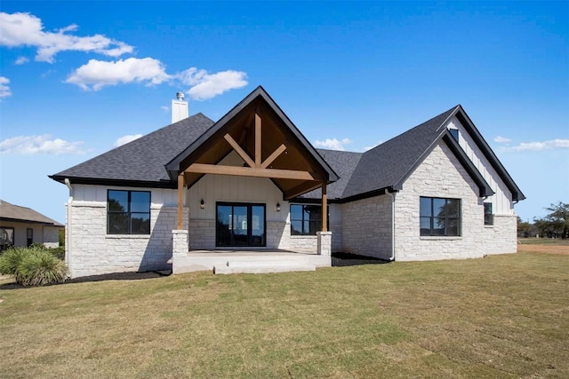 rear view of property featuring a lawn, roof with shingles, board and batten siding, a chimney, and a patio area