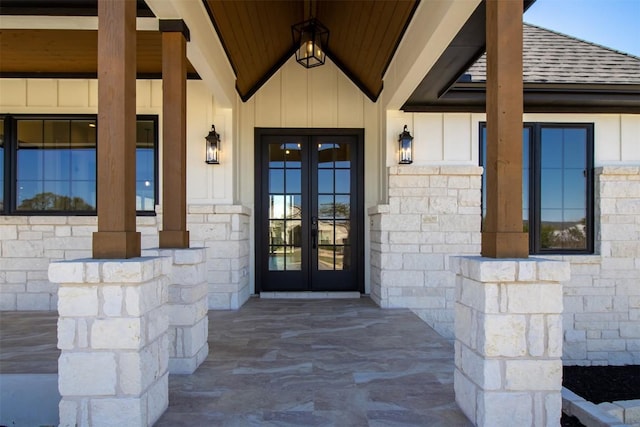 entrance to property featuring board and batten siding, french doors, stone siding, and roof with shingles