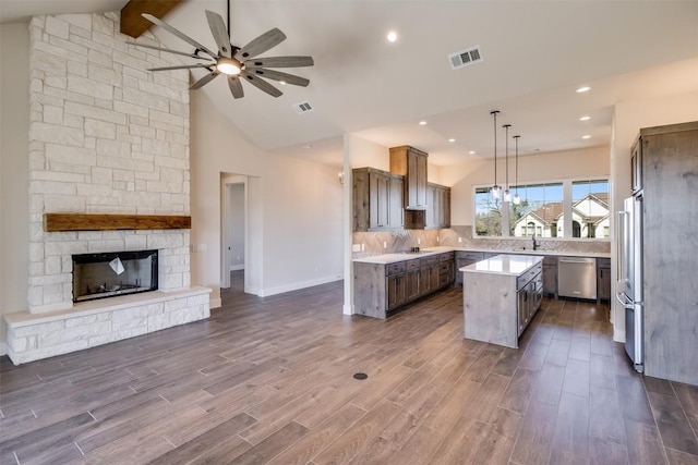 kitchen with visible vents, a kitchen island, a stone fireplace, appliances with stainless steel finishes, and open floor plan