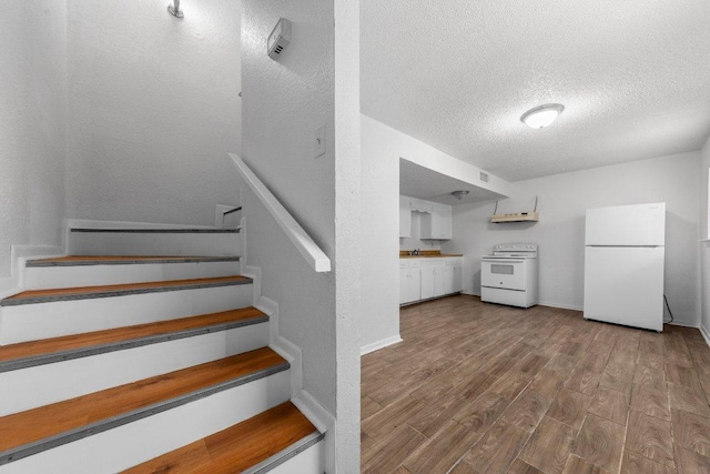 staircase featuring wood finished floors, baseboards, and a textured ceiling