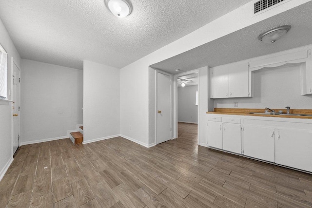 kitchen featuring wood finished floors, baseboards, visible vents, a sink, and white cabinetry