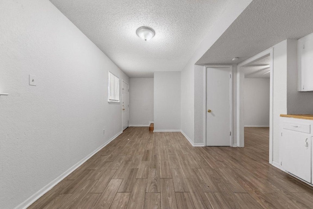 below grade area featuring wood finished floors, baseboards, a textured wall, and a textured ceiling