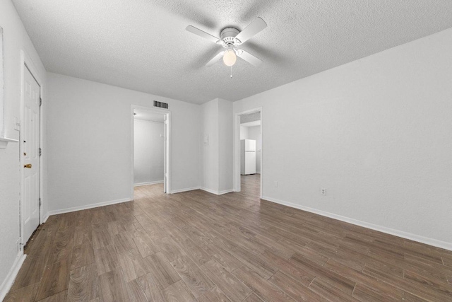 empty room featuring visible vents, baseboards, wood finished floors, a textured ceiling, and a ceiling fan