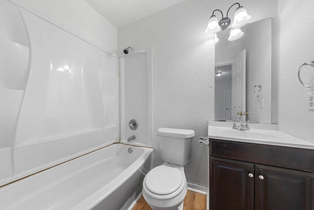 full bath featuring vanity, washtub / shower combination, toilet, and a textured wall