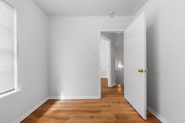 spare room featuring a textured ceiling, baseboards, and light wood-style floors