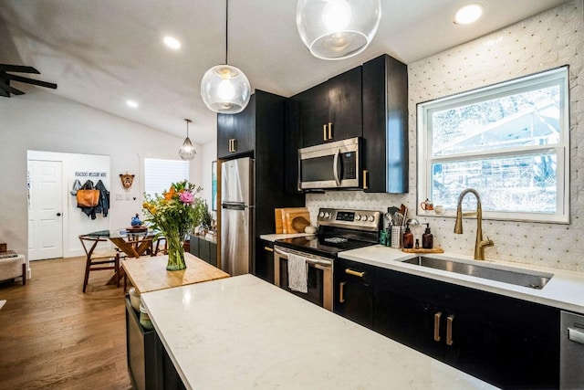 kitchen with dark cabinetry, a sink, stainless steel appliances, vaulted ceiling, and light countertops