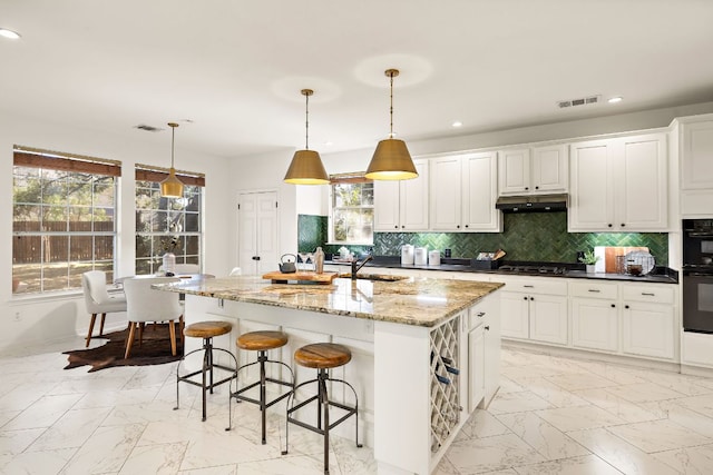 kitchen featuring visible vents, gas stovetop, under cabinet range hood, marble finish floor, and backsplash