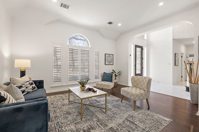 living room featuring arched walkways, visible vents, lofted ceiling, and wood finished floors