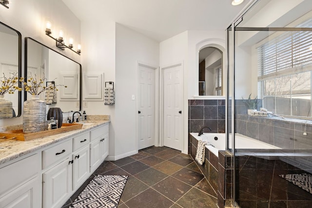 full bathroom featuring a bath, vanity, baseboards, and stone tile flooring