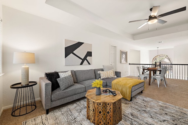 carpeted living room with baseboards, a raised ceiling, and ceiling fan