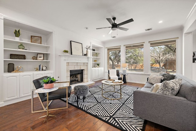 living room featuring visible vents, built in shelves, dark wood-type flooring, a ceiling fan, and a fireplace