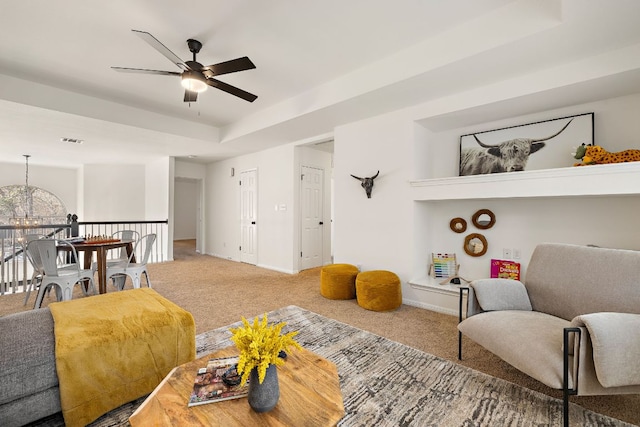 living room with carpet, visible vents, baseboards, a raised ceiling, and ceiling fan with notable chandelier