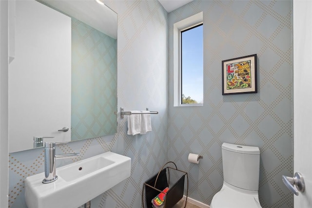 half bath with wallpapered walls, toilet, and a sink