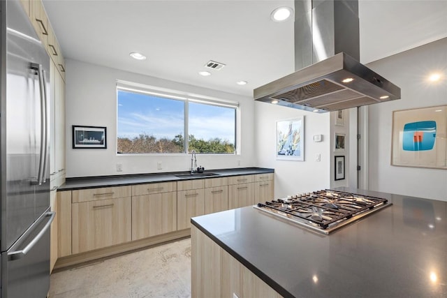 kitchen featuring dark countertops, light brown cabinetry, island exhaust hood, stainless steel appliances, and a sink