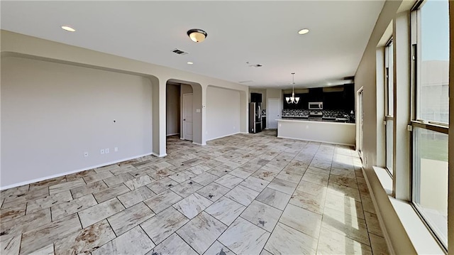 unfurnished living room with recessed lighting, visible vents, arched walkways, and baseboards