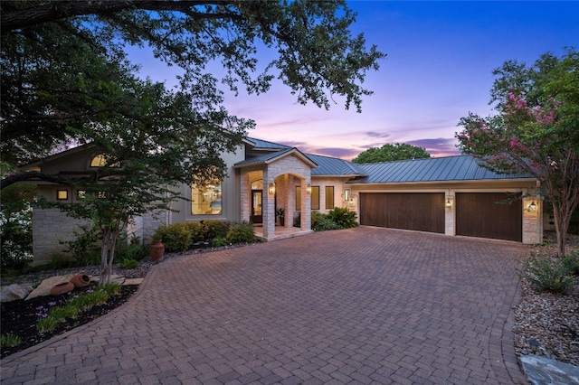 view of front of property featuring a standing seam roof, decorative driveway, stone siding, metal roof, and a garage