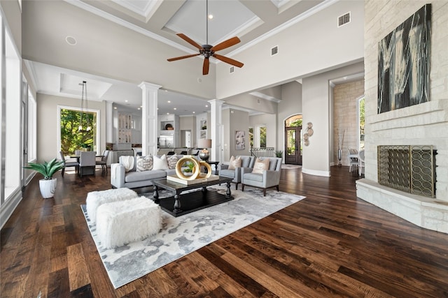 living area with visible vents, a stone fireplace, wood finished floors, coffered ceiling, and ornate columns