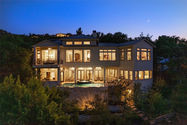 back of property at dusk with a patio, a balcony, stairway, a chimney, and metal roof