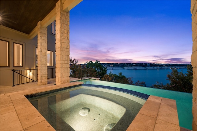 pool at dusk with an in ground hot tub and a water view