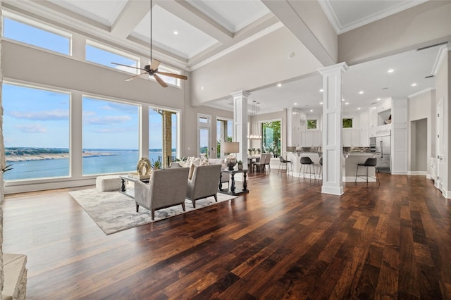 living area with ceiling fan, dark wood-style floors, crown molding, a towering ceiling, and ornate columns