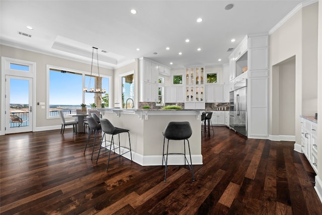 kitchen with a breakfast bar area, a tray ceiling, crown molding, backsplash, and stainless steel built in refrigerator