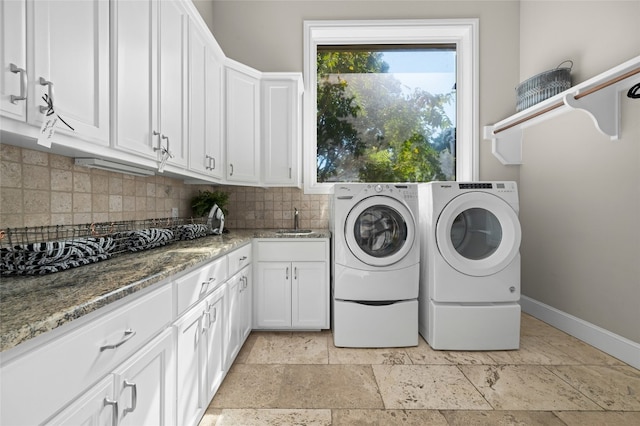 washroom with baseboards, cabinet space, separate washer and dryer, stone tile flooring, and a sink