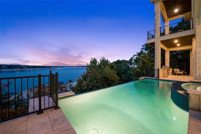 711 Cutlass, Lakeway, TX 78734 - pool at dusk featuring a water view, a pool with connected hot tub, and a patio area