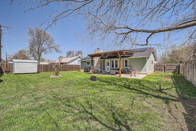 back of property featuring a patio, solar panels, a yard, a fenced backyard, and a chimney